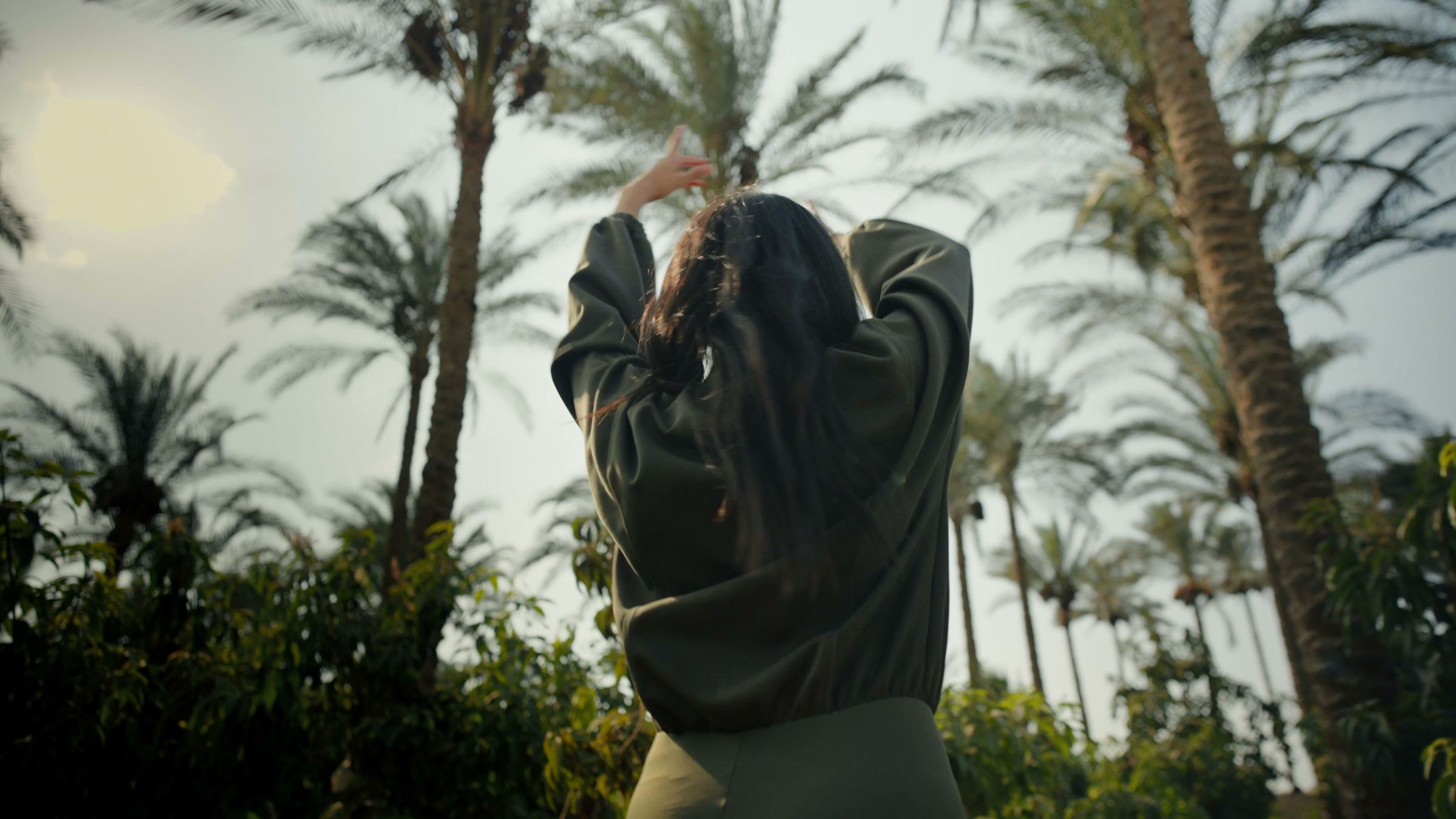 A woman in a ROUH set raising her arms under palm trees in soft evening light